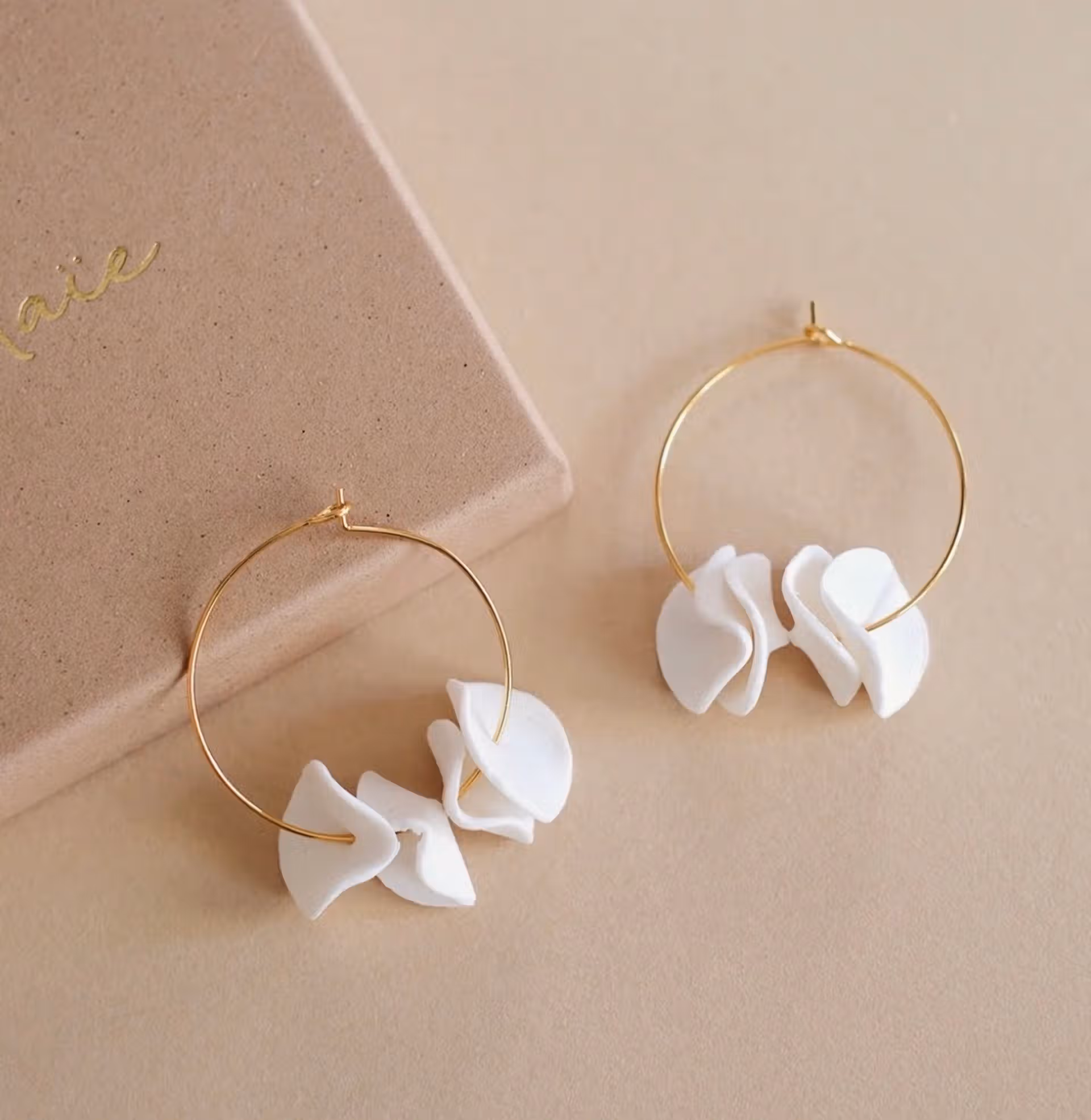 Créoles dorées fines ornées de pétales blancs en argile polymère, boucles d’oreilles artisanales modernes et légères.