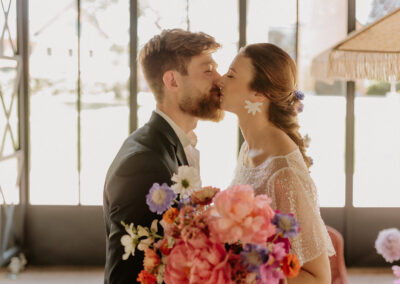 Couple de mariés s’embrassant tendrement lors de leur cérémonie, la mariée tenant un bouquet de fleurs coloré