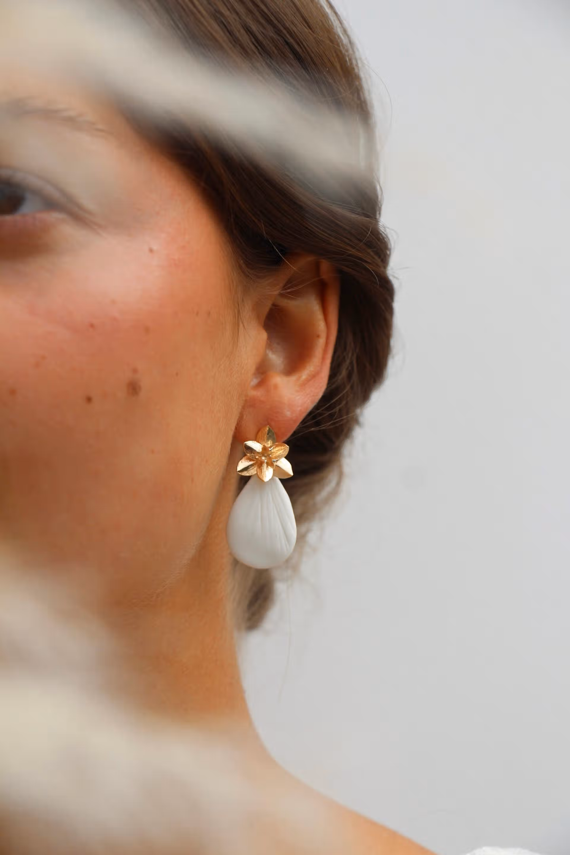 Gros plan du modèle CAMILLE porté, montrant la puce en forme de fleur dorée et le pendentif goutte blanc aspect porcelaine.